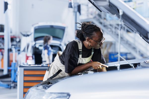 Mechanic in car service picking torque wrench from work station bench, using it to tighten bolts after replacing motor. BIPOC garage worker uses professional tools to fix client automobile